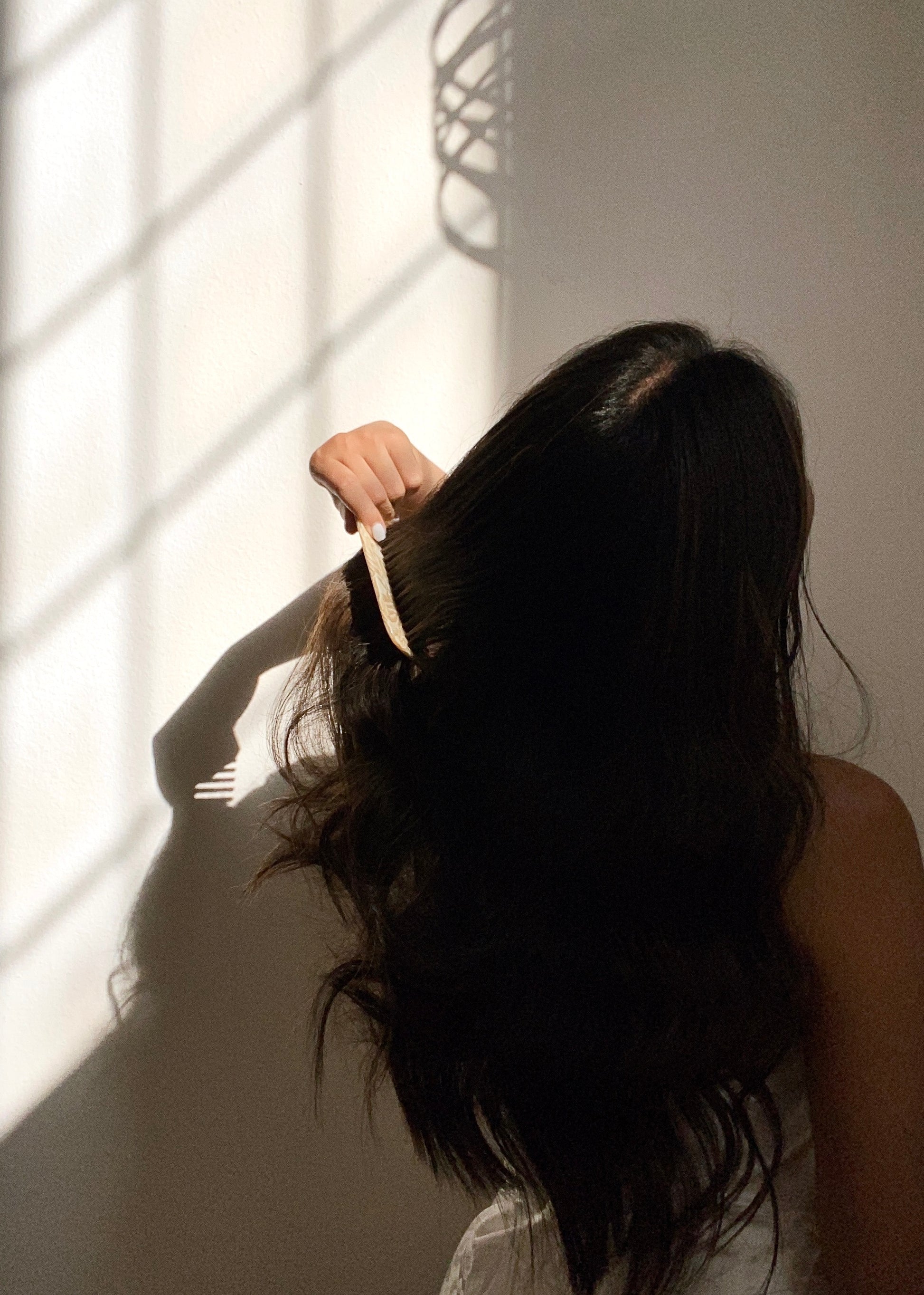 Women combing her hair with marble wide tooth comb under natural indoor sunlight